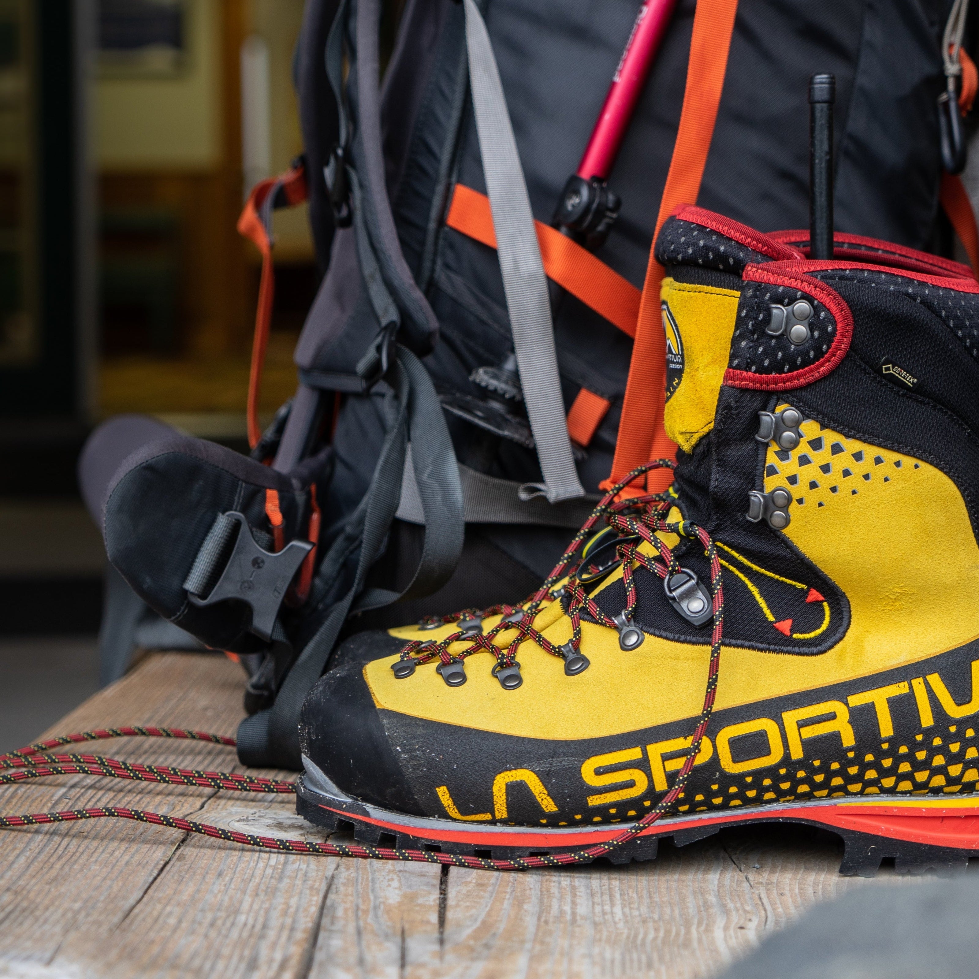 Yellow and black hiking boot with 'La Sportiva' branding on a wooden surface, next to a backpack.