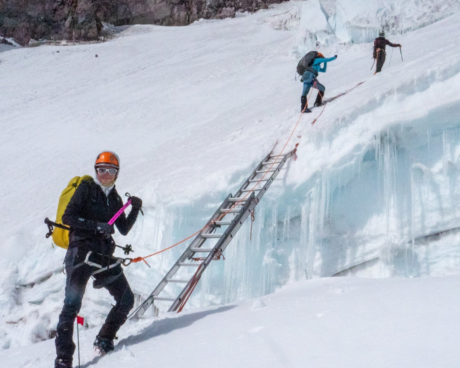 Person climbing a frozen waterfall with a ladder on a snowy mountain